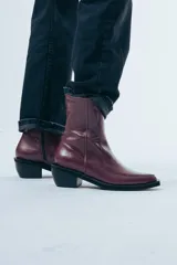 Bota de caña media confeccionada en cuero negro con acabado brillante, diseño de silueta limpia, puntera cuadrada y taco cuadrado de altura media.