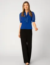 Blusa de color blanco con escote en V y detalle de lazo frontal. Presenta mangas cortas de gasa con terminación en puño.