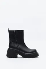 Bota de caña media color negro, con plataforma robusta y suela dentada. Presenta un diseño minimalista con cierre lateral para un calce práctico.