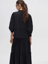 Camisa de broderie de algodón color negro, con diseño de calados, cuello mao con cierre de botones, mangas abullonadas con puños fruncidos y detalles de galones con transparencias.