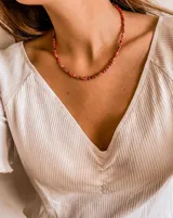 Collar corto de cuentas de vidrio en tonos de rojo y naranja, con pequeñas cuentas plateadas.