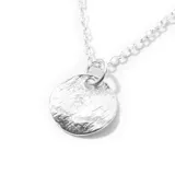 Collar plateado con dije circular texturado.