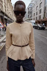 Chaqueta de cuello redondo y manga larga con diseño peplum en el bajo. Confeccionada en tejido efecto ante, cuenta con cierre frontal de cremallera y cinturón fino ajustable en la cintura.