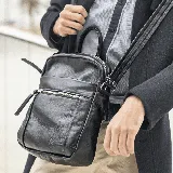 Bandolera negra de cuero vacuno con correa ajustable. Tiene un bolsillo frontal con cierre, un bolsillo frontal abierto y un bolsillo trasero con cierre. El interior está forrado y tiene un bolsillo con cierre y un bolsillo pequeño para el celular.