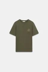 Camiseta de algodón con efecto lavado, cuello redondo y manga corta. Presenta un detalle de fornitura metálica aplicada en el pecho.