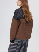 Campera acolchada con diseño de bloques de color en tonos terracota y beige. Presenta cuello camisero y puños en pana negra, cierre frontal oculto con botones a presión y costuras capitoneadas en toda la prenda.