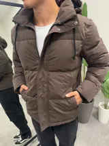 Campera puffer color marrón, con diseño acolchado, capucha forrada y cierre frontal con solapa de botones a presión.