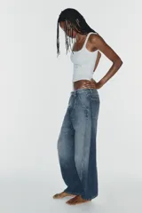 Jeans de tiro medio y corte barrel con diseño de perneras curvadas, tiro medio, trabillas para cinturón y cinco bolsillos. Presenta lavado clásico y costuras pespunteadas decorativas en la parte delantera.