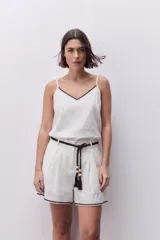 Short de tiro alto de lino color blanco, con pinzas delanteras y detalle de bordado en contraste en el ruedo. Incluye cinturón de cordón trenzado con borlas y cuentas.