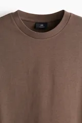 Remera marrón de algodón pesado, corte oversized, con cuello redondo ribeteado, hombros caídos y bajo recto.