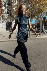 Vestido corto de cuello subido y sin mangas, confeccionado en tejido satinado. Presenta un detalle de fruncido lateral con abertura frontal y aplicación de encaje en el bajo.