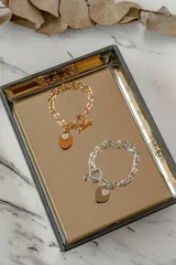 Pulsera de eslabones gruesos en acero quirúrgico color plata, con dijes colgantes en forma de corazón, uno liso y otro con incrustaciones.