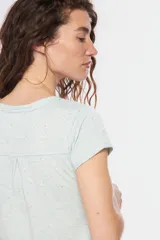 Remera color beige con cuello redondo, mangas cortas, bolsillo pequeño en el pecho y media botonadura frontal.