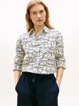 Camisa Tommy Hilfiger de corte amplio confeccionada en lino puro, con diseño estampado de líneas geométricas en azul sobre base blanca. Presenta cuello inglés, cierre frontal abotonado, mangas largas con puños abotonados y logo bordado en el pecho.