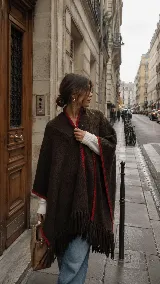 Ruana tejida a mano en lana merino color marrón chocolate, con diseño envolvente, flecos en el ruedo y detalle de guarda artesanal en color rojo en los bordes.