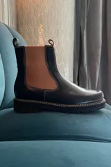 Bota Chelsea de cuero negro con elástico lateral marrón acanalado, suela track y tirador trasero.