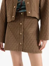 Pollera mini de pana con diseño matelaseado en forma de rombos, color marrón. Presenta una cartera frontal con botones dorados funcionales.