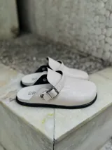 Zueco negro de cuero sintético con textura, estilo cerrado y tira ajustable con hebilla metálica plateada.