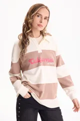 Buzo deportivo sin friza a rayas anchas en tonos blanco y tostado, con cuello polo, escote en V y estampa frontal con la inscripción "California est.1969" en color fucsia. Presenta un corte semi oversize y mangas largas.