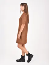 Vestido corto de corte recto y estilo minimalista, confeccionado en tela tipo gamuza negra. Presenta cuello redondo, mangas cortas y dos bolsillos frontales aplicados a la altura de la cadera.