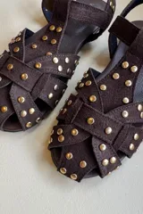 Sandalia tipo guillermina confeccionada en cuero nobuk color chocolate, con diseño de tiras cruzadas y tachas doradas decorativas.