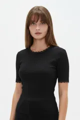 Remera de algodón negro con textura acanalada, manga corta y cuello redondo base. Presenta sutiles detalles de puntilla en el cuello y en los bordes de las mangas.