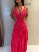 Vestido largo fucsia con aberturas cut-out en la cintura, escote halter con tiras cruzadas y detalles de encaje y plisado en el corpiño y la falda.
