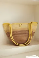 Bolso de mano tipo tote, confeccionado en soga de algodón con diseño a rayas horizontales en degradé de color marrón y beige. Asas de hombro amarillas y cierre con broche de bronce.