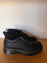 Borcego negro de cuero con cordones, suela track y detalle de costuras amarillas.