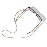 Correa para lentes marca Meller, confeccionada en cuero sintético color marrón con detalles metálicos en tono dorado. Incluye terminales de silicona ajustables para sujetar las gafas y un dije circular con el logo de la marca grabado.
