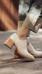 Zapato de cuero color beige, con taco de madera y suela dentada. Presenta un diseño slip-on con detalles de textura en relieve en los laterales y el empeine.