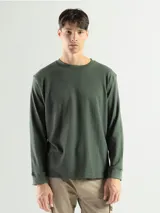 Remera de manga larga con cuello redondo, confeccionada en tejido de algodón tipo mini piqué. Presenta un diseño versátil con puños elásticos en las mangas, ideal para usar como prenda base o como buzo ligero.