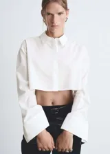 Camisa crop de popelín con cuello camisero, cierre frontal de botones ocultos y mangas largas con puños anchos abotonados.