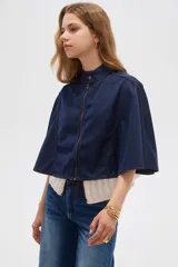 Poncho corto de denim azul con cuello alto, cierre frontal y diseño amplio de inspiración capa.