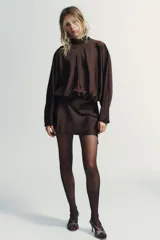Vestido corto de tejido satinado color marrón chocolate, con cuello subido y lazada tipo foulard integrada. Presenta mangas largas amplias, detalle de frunces en la cintura y cierre lateral con cremallera oculta.