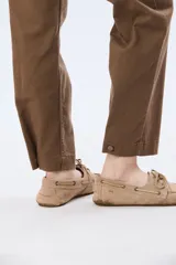 Pantalón de gabardina marrón, de corte recto con pinza en el bajo y detalles de botones en los tobillos.