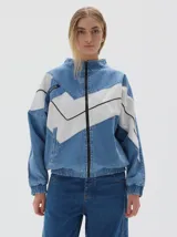 Campera de jean estilo deportivo con cierre frontal, cuello alto y diseño de paneles en forma de V en color blanco. Presenta corte oversized, puños y cintura elásticos, y bolsillos frontales con cierre.