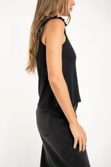 Remera negra de viscosa y elastano, con cuello redondo y mangas cortas con volados. Tiene un corte holgado y un pequeño detalle metálico dorado en el bajo.