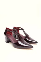 Sandalia de cuero color bordó, con acabado charolado, punta fina y tacón cuadrado de 5 cm. Presenta una tira en forma de T sobre el empeine y una correa con hebilla alrededor del tobillo.