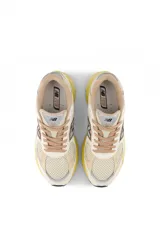 Championes New Balance modelo 2010, con capellada en tonos crema, beige y amarillo pastel. Presentan malla transpirable, superposiciones de gamuza y detalles en azul claro en el logo 'N'. La entresuela es voluminosa y de color amarillo translúcido.