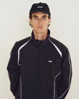 Campera tipo rompevientos de la marca Obey, con diseño a cuadros pequeños en tonos azul y blanco. Presenta cuello alto, cierre frontal completo, bolsillos laterales y detalles de líneas negras contrastantes que recorren el frente y las mangas. Incluye el logo de la marca bordado en el pecho.