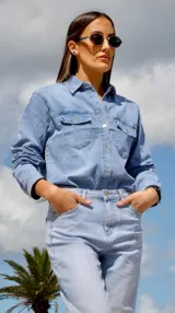 Camisa de jean celeste con cuello clásico, calce entallado, cierre frontal con botones metálicos y doble bolsillo con solapa abotonada en el pecho.