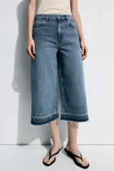 Bermuda larga de jean color azul, tiro medio, con diseño wide leg y bolsillos. Cuenta con bajo desflecado y cierre frontal con cremallera y botón metálico.