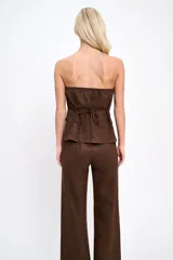 Conjunto de dos piezas confeccionado en tela agamuzada. Incluye un top strapless con cierre frontal de botones y bolsillos decorativos, y un pantalón de corte recto y tiro alto.