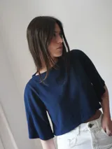 Top corto azul marino de punto, con mangas cortas amplias, cuello redondo y detalle de escudo bordado en la parte delantera.