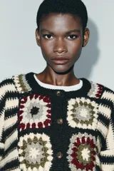 Chaqueta de punto con cuello redondo y manga larga, que combina un diseño de rayas horizontales en blanco y negro con paneles frontales decorados con motivos de crochet en tonos tierra y granate. Presenta cierre frontal con botones.