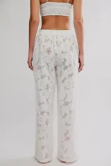 Pantalón blanco de algodón con diseño de bordados tipo broderie con motivos florales, corte holgado de pierna ancha, tiro medio con cintura elástica y cordón ajustable.