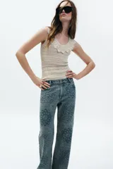 Jeans de tiro alto con corte flare y diseño de tejido jacquard con patrón floral. Presenta cinco bolsillos, trabillas en la cintura y cierre frontal con cremallera y botón.