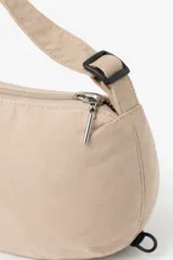 Bandolera color beige, con forma rectangular y extremos redondeados. Tiene una correa ajustable con hebilla negra y cierre de cremallera en la parte superior.