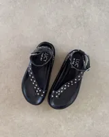 Sandalia tipo ojota con plataforma, color negro, con tiras decoradas con tachas metálicas plateadas y ajuste en el tobillo con hebilla.